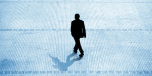 Silhouette of a businessperson walking on a tiled outdoor plaza with their shadow cast on the ground, symbolizing professional advancement and entrepreneurship.