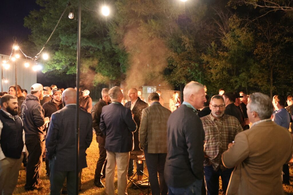 People attending outdoor networking event at night, string lights, social gathering, professional event, evening meet and greet, corporate networking, outdoor party, night-time event, business social, casual professional attire.