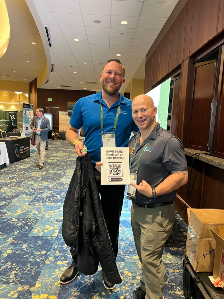 Smiling conference attendees holding a QR code sign for mobile registration at the Global Sports Federation event.