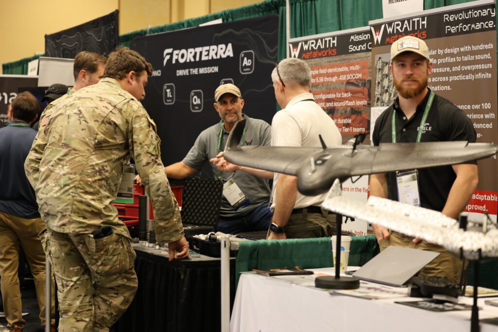- Military personnel and industry representatives discussing drone technology at a trade show booth.